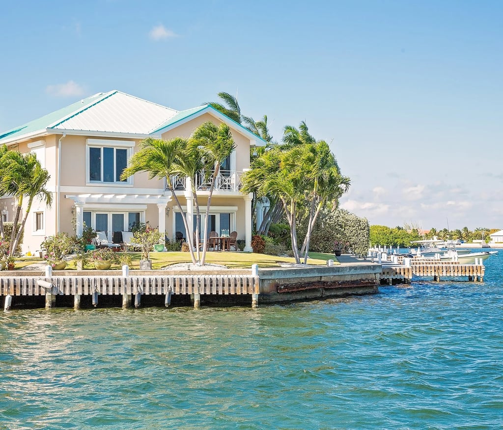Luxury waterfront tropical villa with palm trees and a private boat dock on blue water.