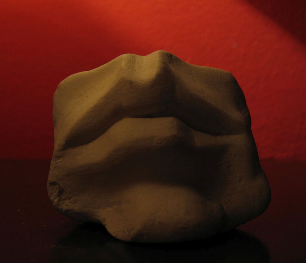 Poljubac. Figura od gline, usne na crvenoj pozadini.