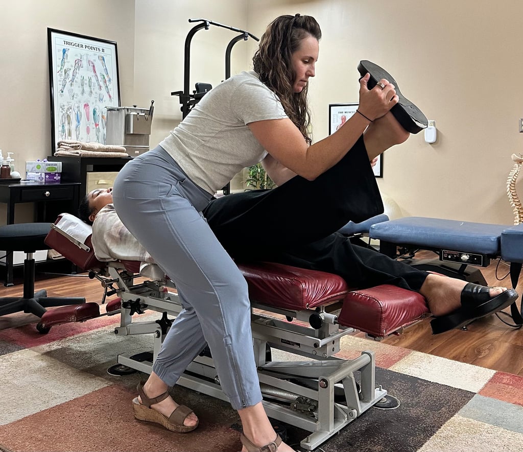 Chiropractor performing nerve tension test on patient laying face up on chiro table.