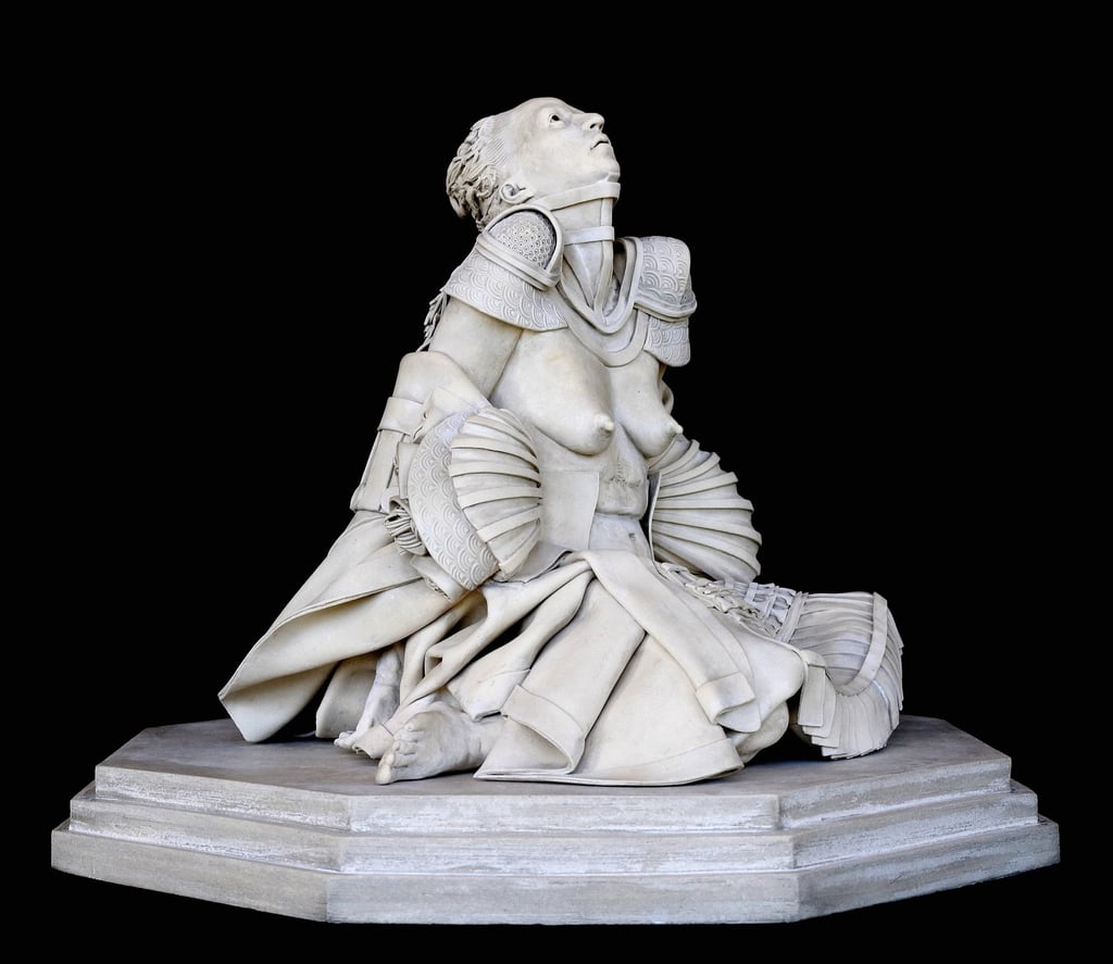 Ceramic sculpture of fallen nude woman pleading upward, with flowing robe, shells, samurai skirt, shoulder armor, neck brace.