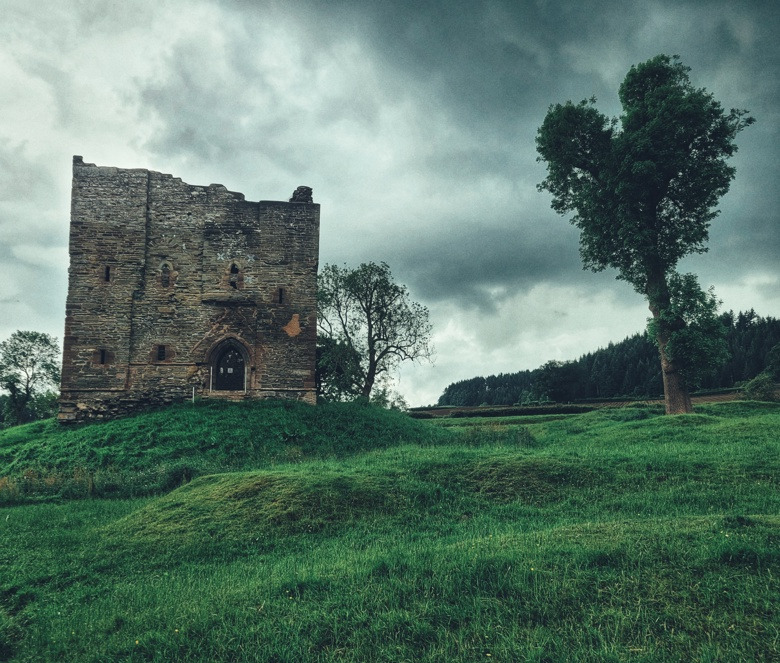 Historic stone castle ruins standing on a green hill under a dramatic cloudy sky.
