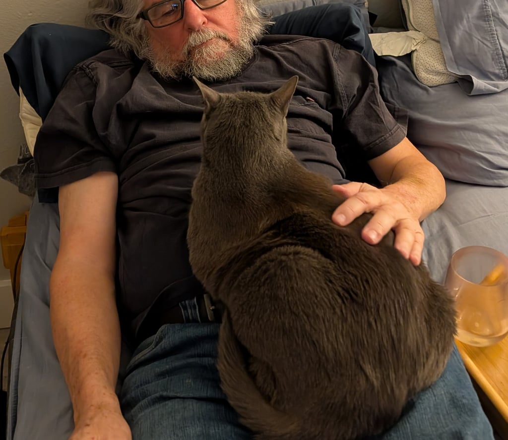 Greg Rowland lying in bed with his cat, big bit