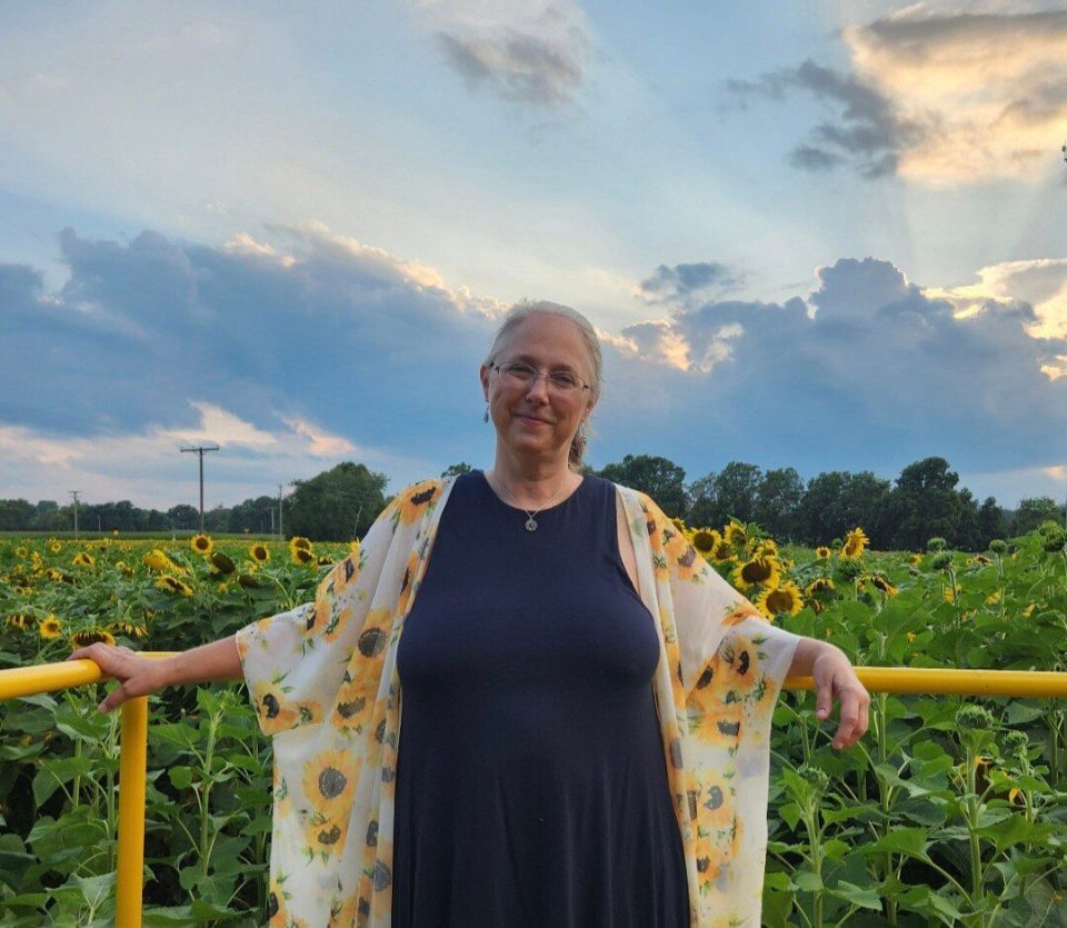 Woman leaning against a fence in a sunflower field.