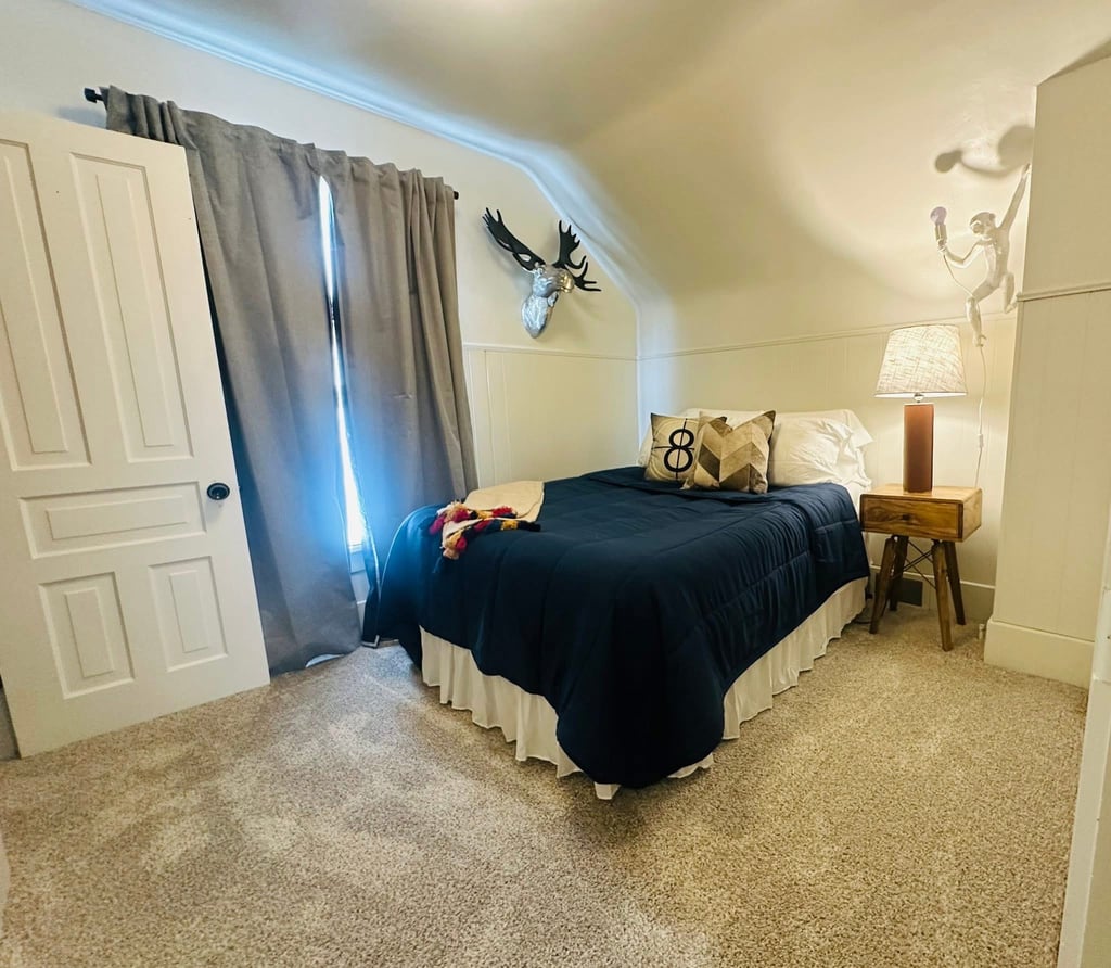 Cozy bedroom with a navy blue bed, silver moose head wall decor, and a wooden nightstand.