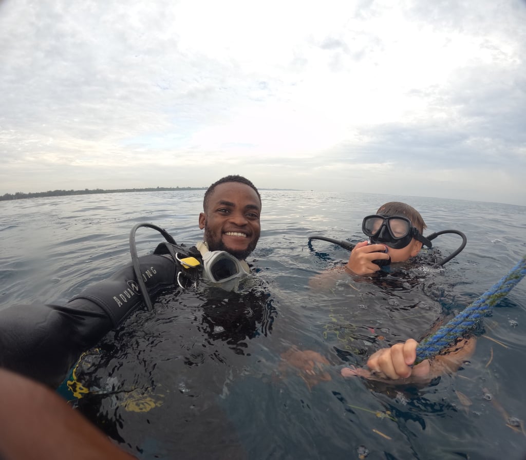 A smiling man and young boy wearing scuba diving gear floating on the ocean surface during a dive excursion.