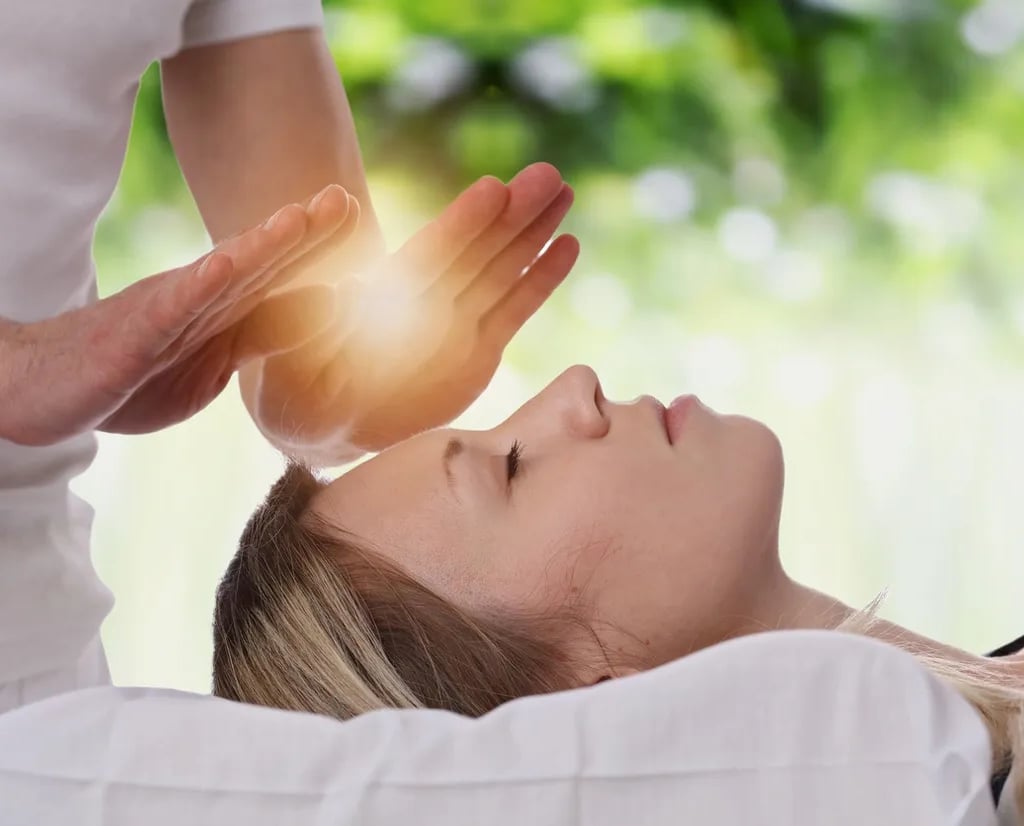 Hands of Reiki Practitioner beaming golden-white  light to a woman's forehead who is laying down