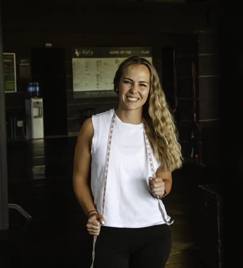 blond woman standing with white top and black exercise pants holding measurement band around her in hands