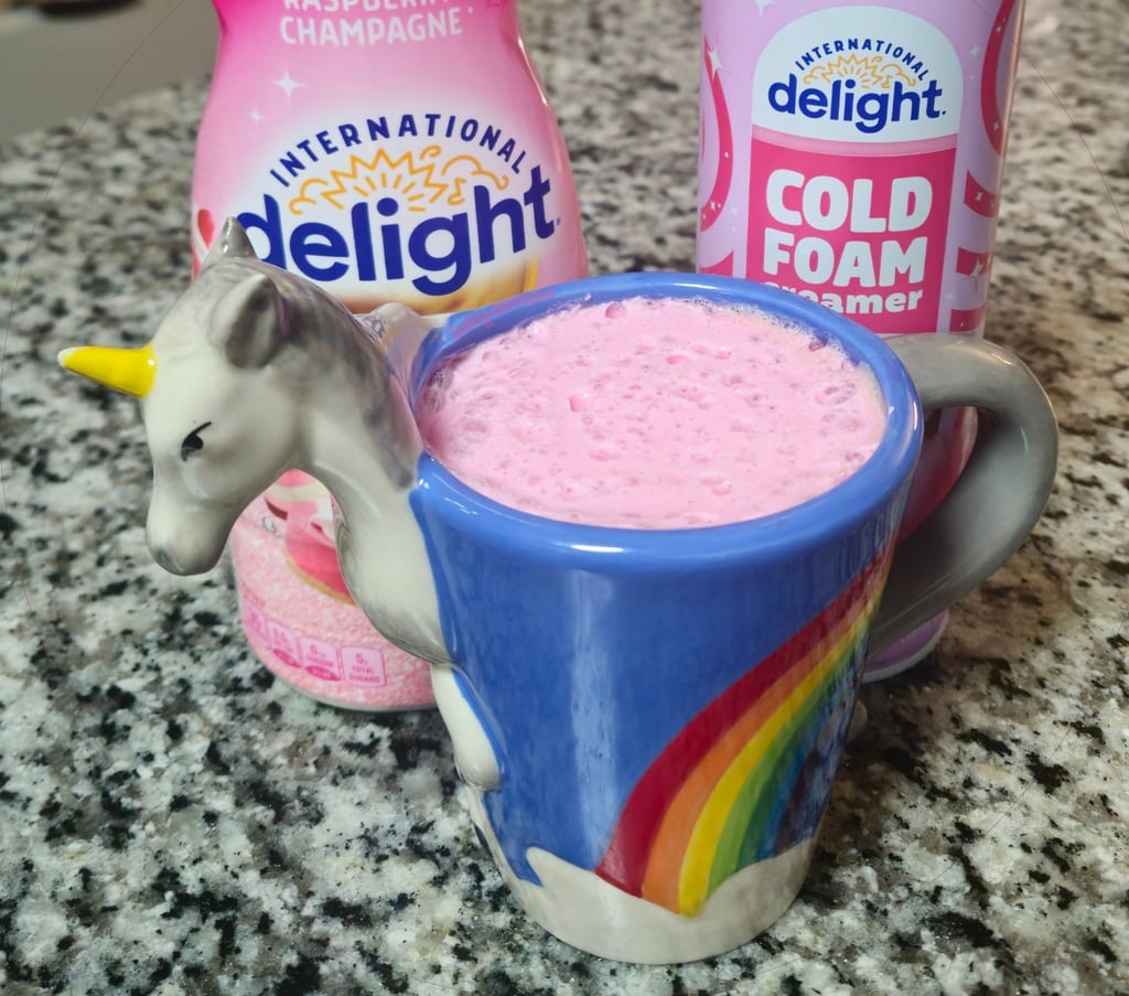 A picture a coffee mug shaped like a unicorn. Inside the mug shows pink cold foam.