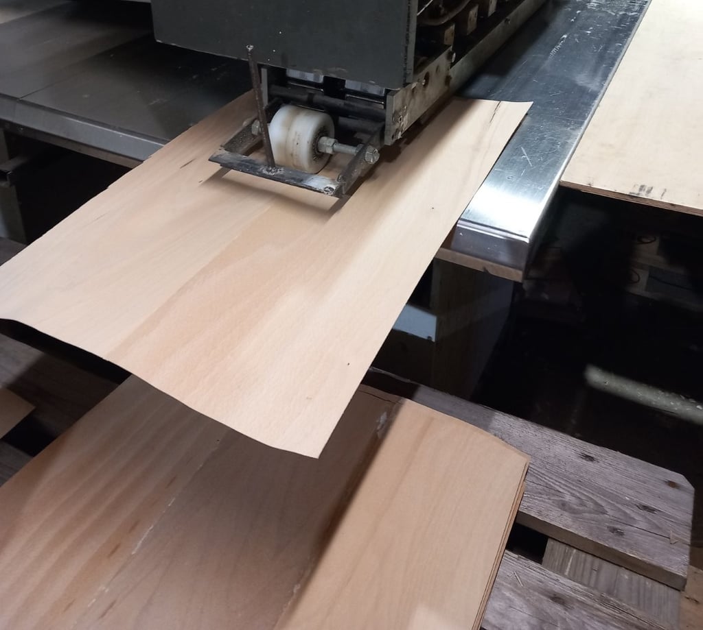Industrial woodworking machine processing thin wood veneer sheets for furniture manufacturing.