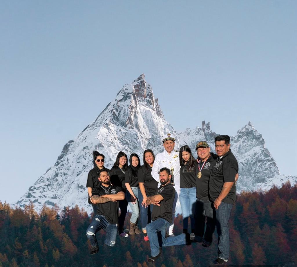 A group of smiling friends posing for a portrait in front of a snowy mountain peak.