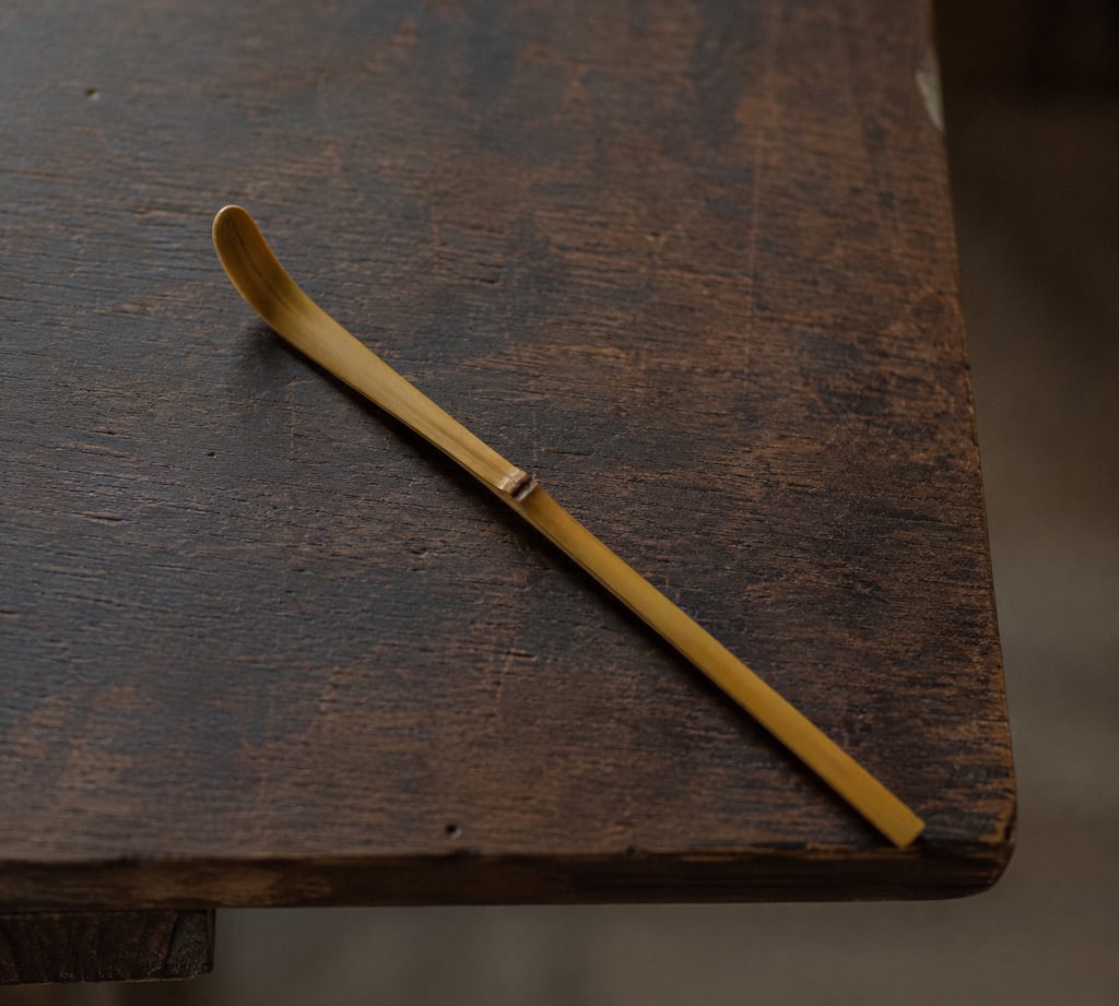 Traditional bamboo matcha tea scoop or chashaku on a rustic dark wooden table.