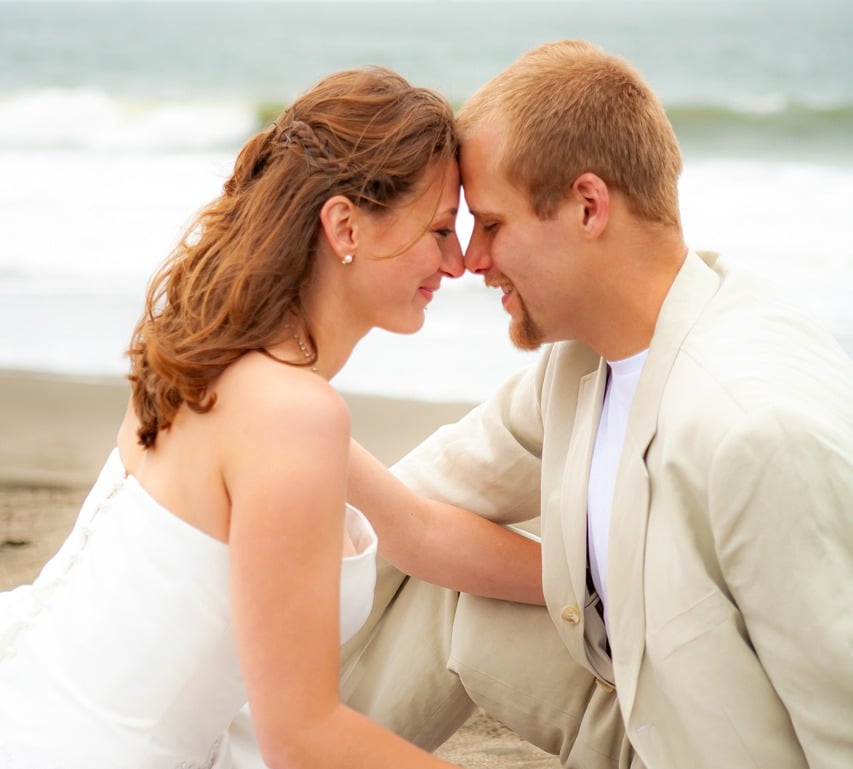 bride and groom, beach photoshoot, sand, ocean, bouquet, sitting
