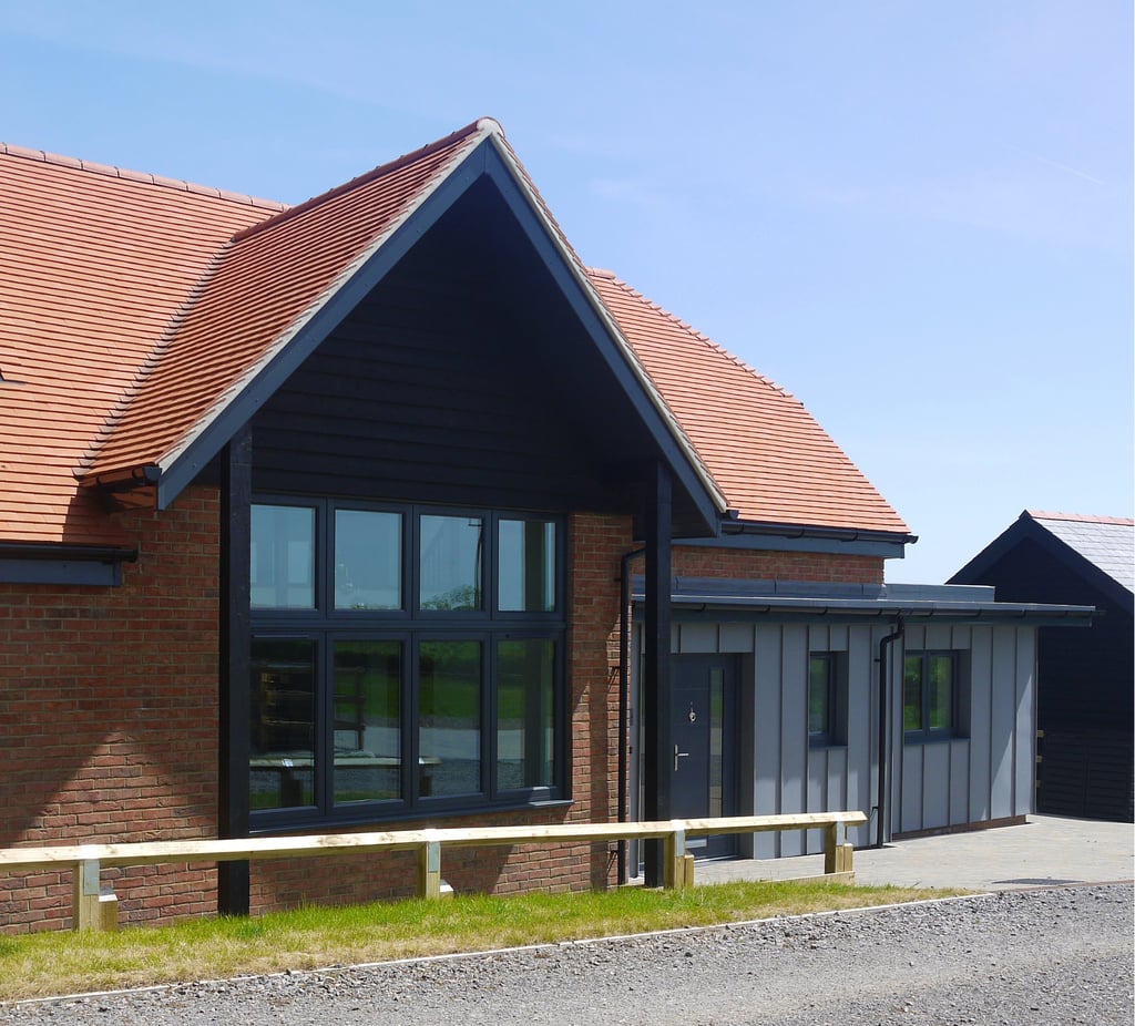 Modern red brick house with a black gabled roof, large windows, and grey zinc cladding extension.
