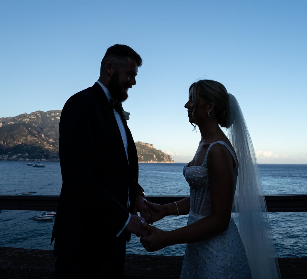 a bride and groom standing on a balcony overlooking the ocean