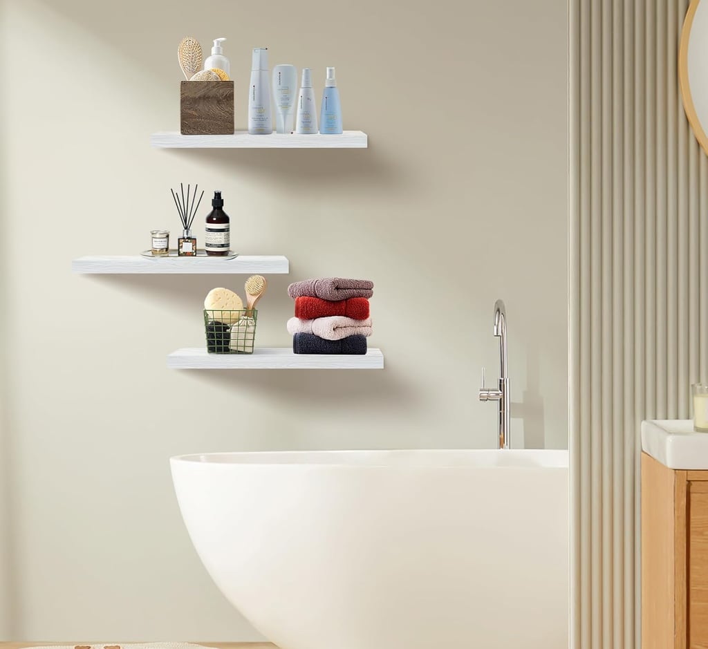 Modern white floating shelves installed above a white bathtub holding skincare products and folded towels.
