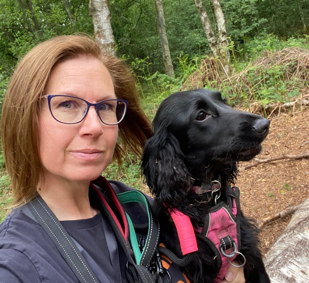 A dog trainer and her black cocker spaniel sit together on a log during a walk