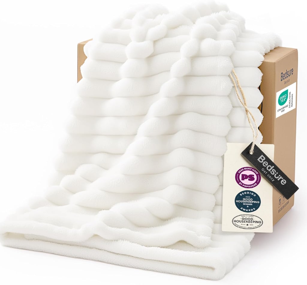 White faux fur throw blanket draped over a cardboard box, featuring a soft ribbed texture and brand tags.