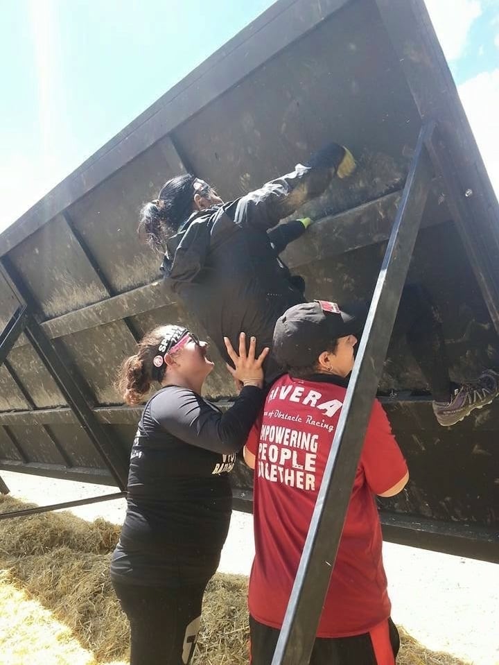 Members of women of racing helping female athlete over inverted wall