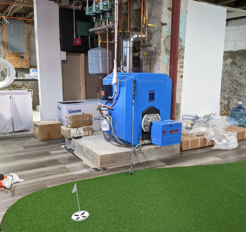 Buderus blue oil boiler system installed in a basement next to an indoor putting green.