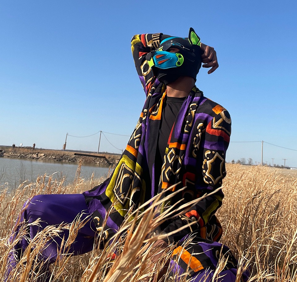 A man in a pup mask posing in a field by the side of a pond.