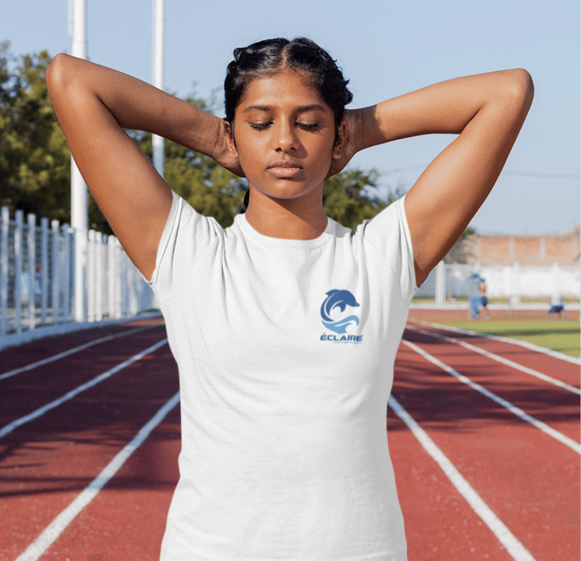 Young woman stretching in a white branded t-shirt on a red running track at an outdoor stadium.