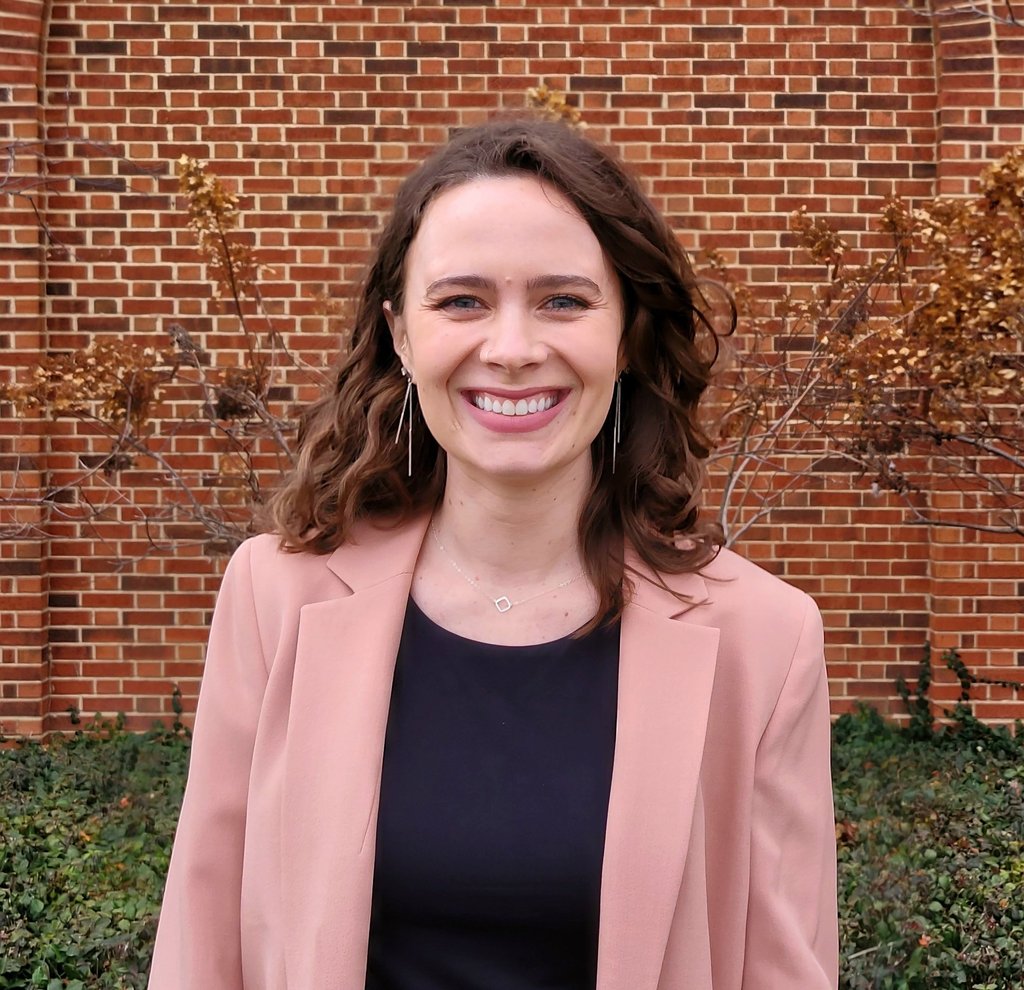 Smiling professional woman in a blazer standing in front of a red brick wall.
