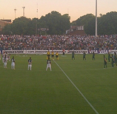 Estádio do Libertad em Assunção antes de jogo da Libertadores, com arquibancadas e gramado iluminado à noite.
