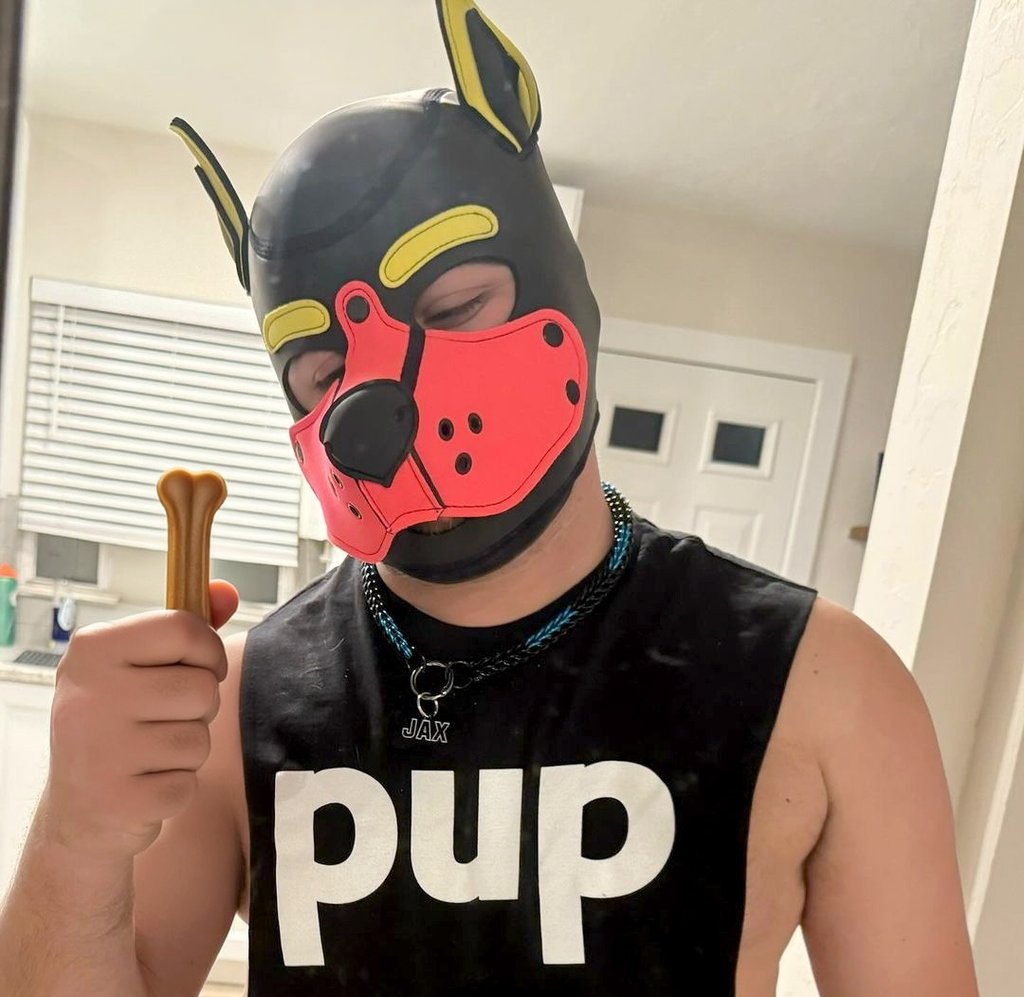 Man in pup mask and t-shirt holding a doggie rawhide chew.