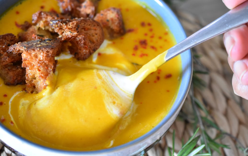 a person holding a spoon and in a bowl of soup