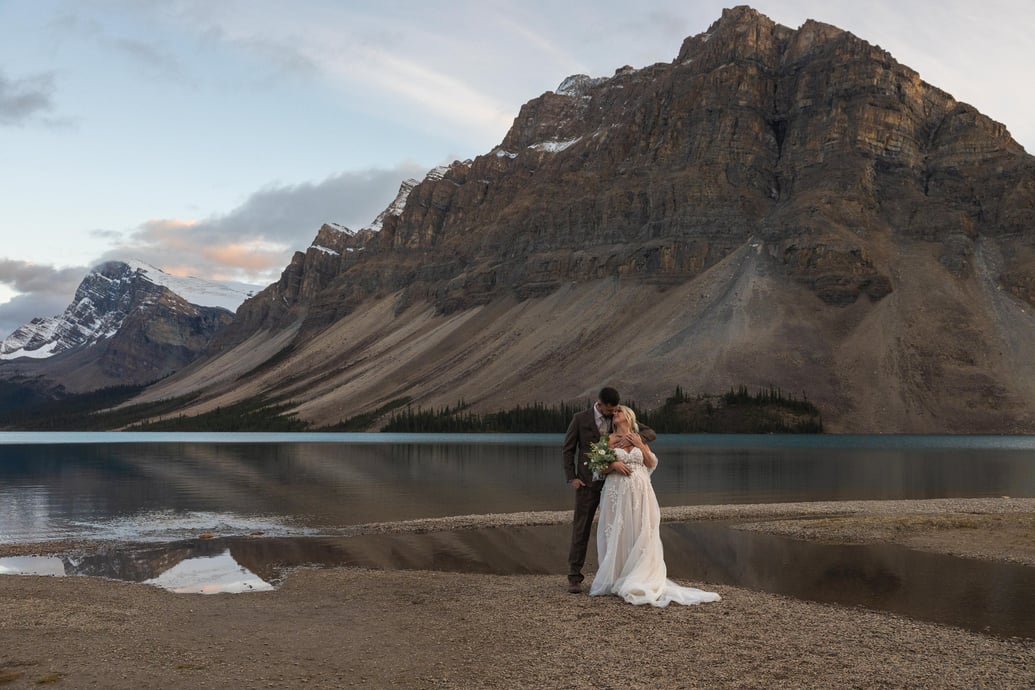 a bride and groom standing in front of Bow Lake in Banff