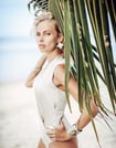 Close-up of a woman in a white bodysuit, large star earrings against a palm leaf background.