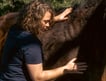 Gemma with her hands on a bay horse putting light pressure on its withers and upper leg.