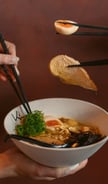 a person holding chopsticks in a bowl of soup