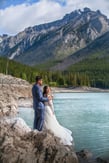 a bride and groom standing on a rock formation at lake minnewanka