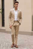 A tailored blue suit jacket draped over a vintage brown leather suitcase, visible through a glass display. The stitching on the jacket is evident, suggesting it is in a bespoke tailoring process. The reflections and lighting create a sophisticated and timeless feel.