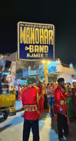 The Manohar Brass Band signboard banner illuminated at night, adding a vibrant touch to the surroundings.