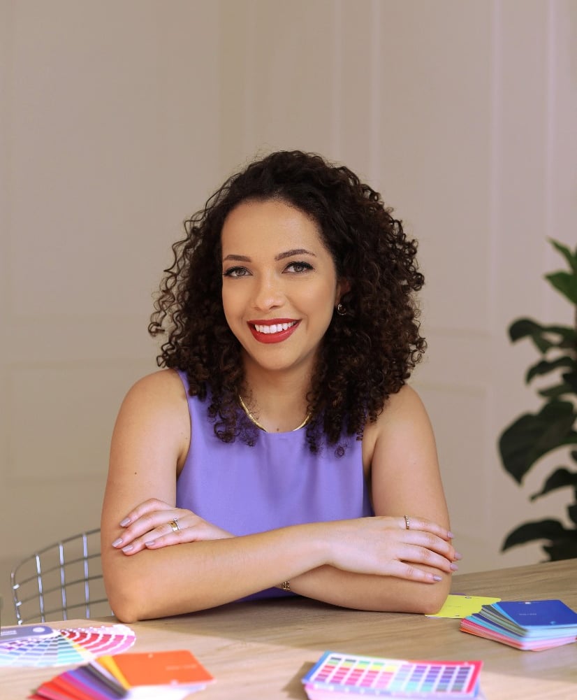 Mulher cacheada sorridente com braços cruzados, oferecendo serviços de coloração pessoal