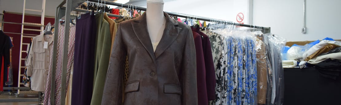 Maniquí con chaqueta corta de polipiel marrón. Fondo con perchas con ropa