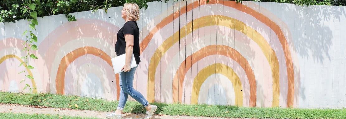 a woman walking down a sidewalk with a laptop in front of a wall