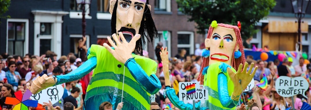 2 Giant puppets wearing yellow reflector vests used in the Amsterdam Pride one is covering mouth