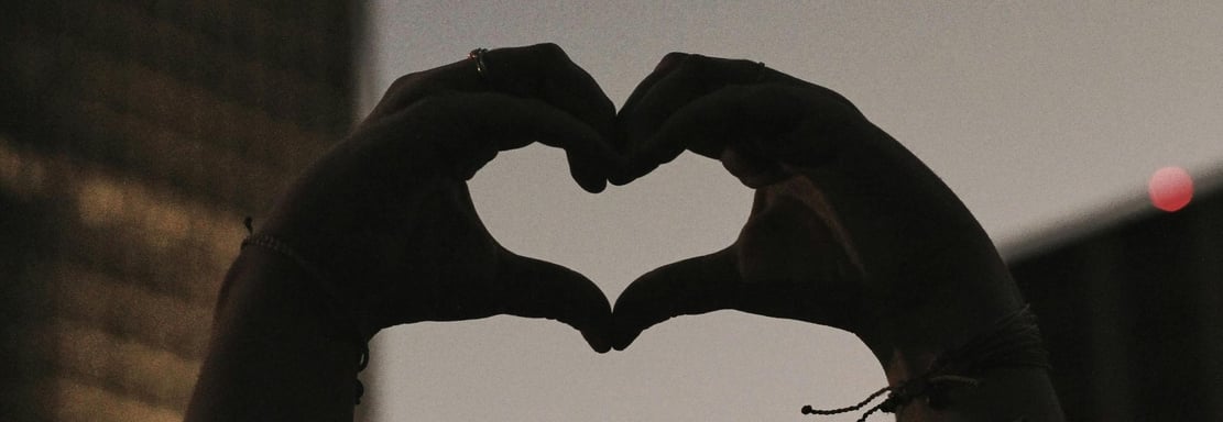 hands forming a heart in front of a building