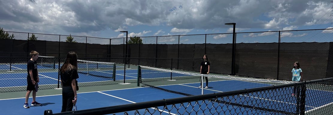 Group of kids playing pickleball on outdoor courts during a Smart Dinker youth session.