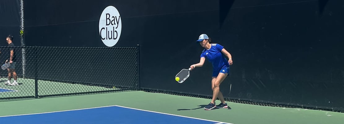 Pickleball player in blue outfit reaching for a low shot during pickleball training match.