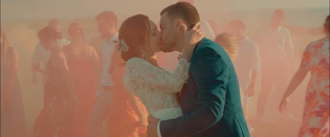 Baiser des mariés capté au milieu d’un décor coloré et vivant avec les invités en mouvement