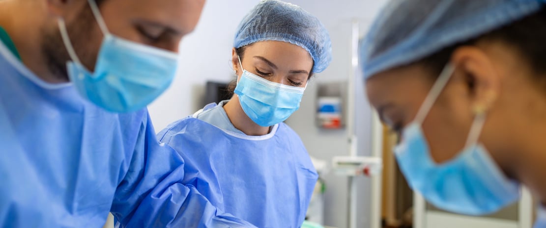 Three surgeons in blue scrubs and masks are focused on a surgical operation in operating room