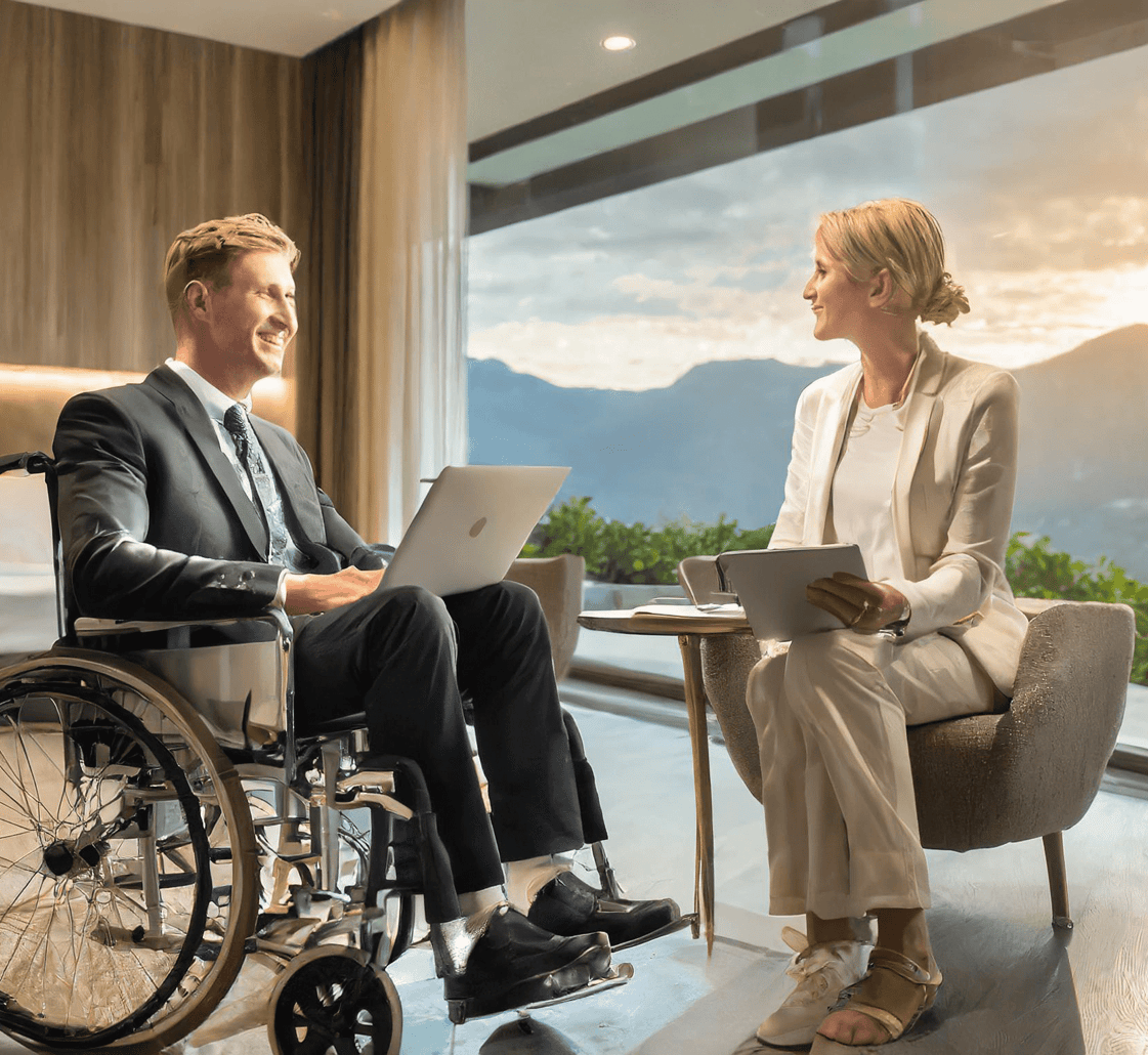Rollstuhlfahrer sitzt einer Dame bei einem Beratungsgespräch in einem Hotelzimmer gegenüber