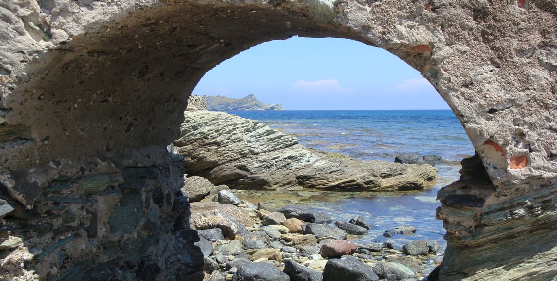 Arcade rocheuse en forme de rond par lequel on aperçoit des rochers et la mer toute bleue