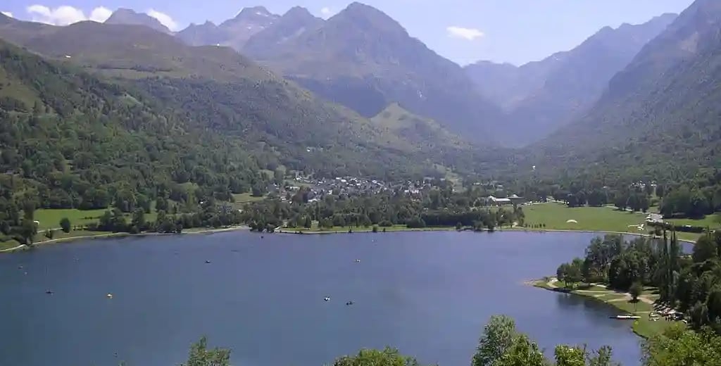 Lac bordé de bois en premier plan et village de Genos en arrière plan au pied des montagnes