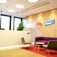 recepcion oficinas Lilly con mueble de recepcion en Corian y sofa y sillas bajas. Pared revestida en madera