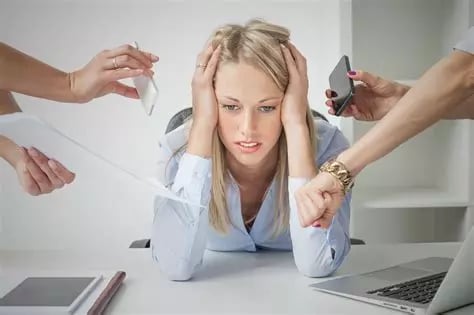 Femme blonde de face stressée se tient la tête à 2 mains et penchée en avant